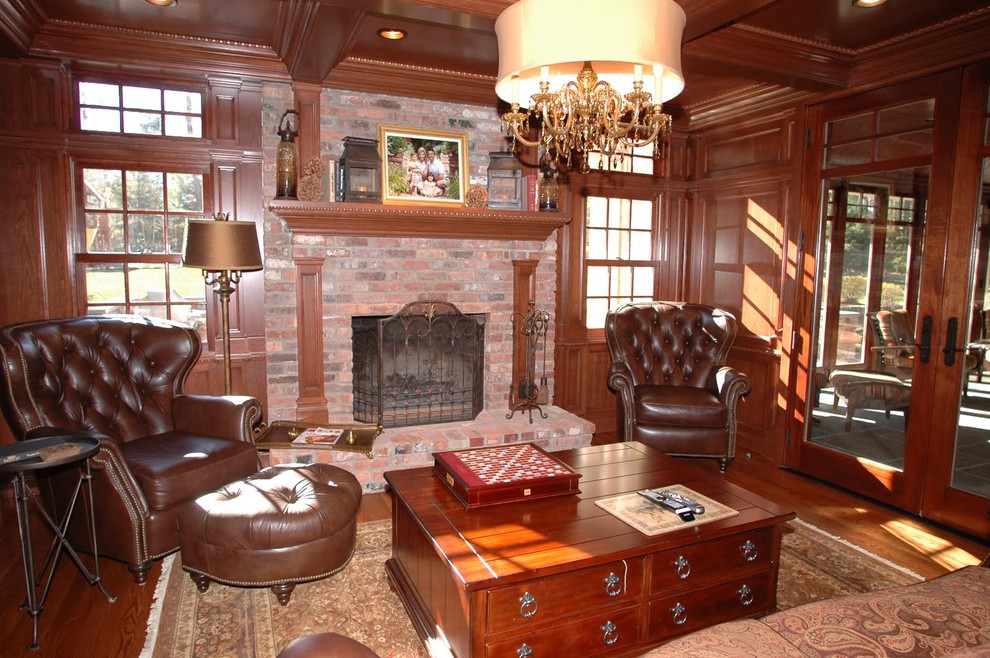 Modelo de sala de estar con biblioteca cerrada clásica grande con suelo de madera en tonos medios, todas las chimeneas, marco de chimenea de ladrillo y pared multimedia