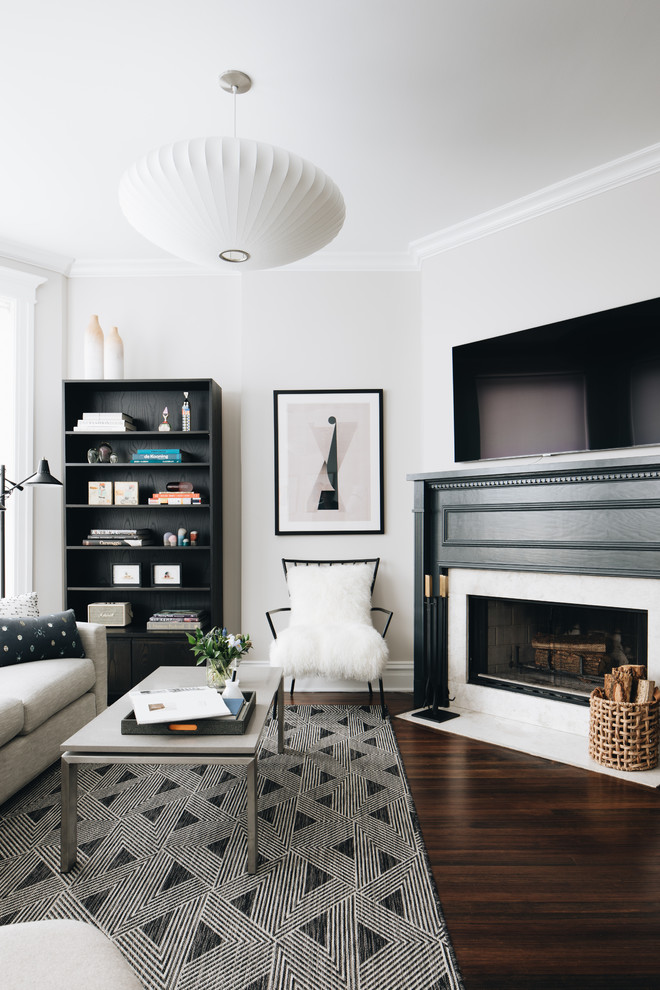 Modelo de sala de estar con biblioteca costera con paredes grises, suelo de madera oscura, chimenea de esquina, marco de chimenea de piedra y televisor colgado en la pared