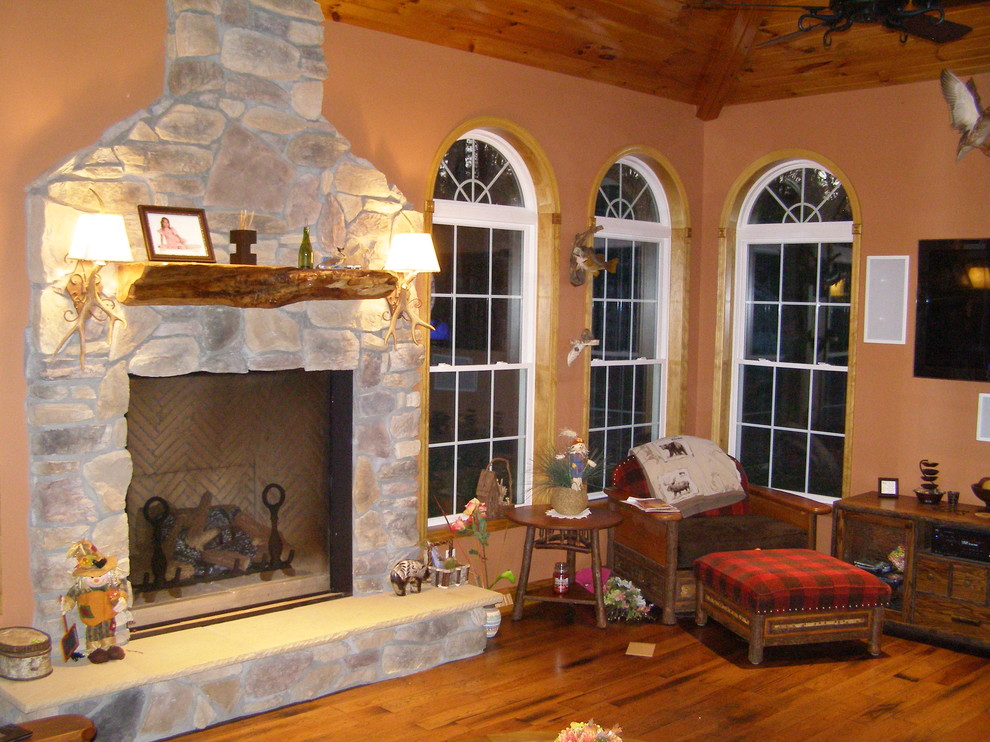Foto de sala de estar cerrada rural de tamaño medio con parades naranjas, suelo de madera en tonos medios, todas las chimeneas, marco de chimenea de piedra y televisor colgado en la pared