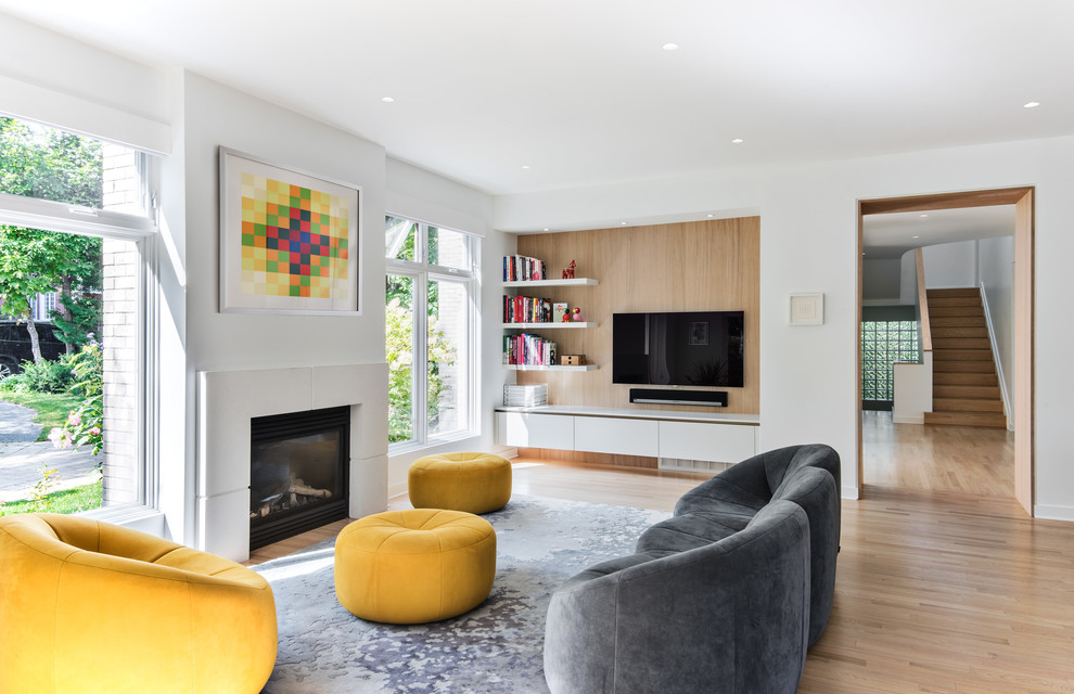 Cette image montre une salle de séjour design avec une bibliothèque ou un coin lecture, un mur blanc, parquet clair, une cheminée standard, un manteau de cheminée en métal, un téléviseur fixé au mur et un sol beige.