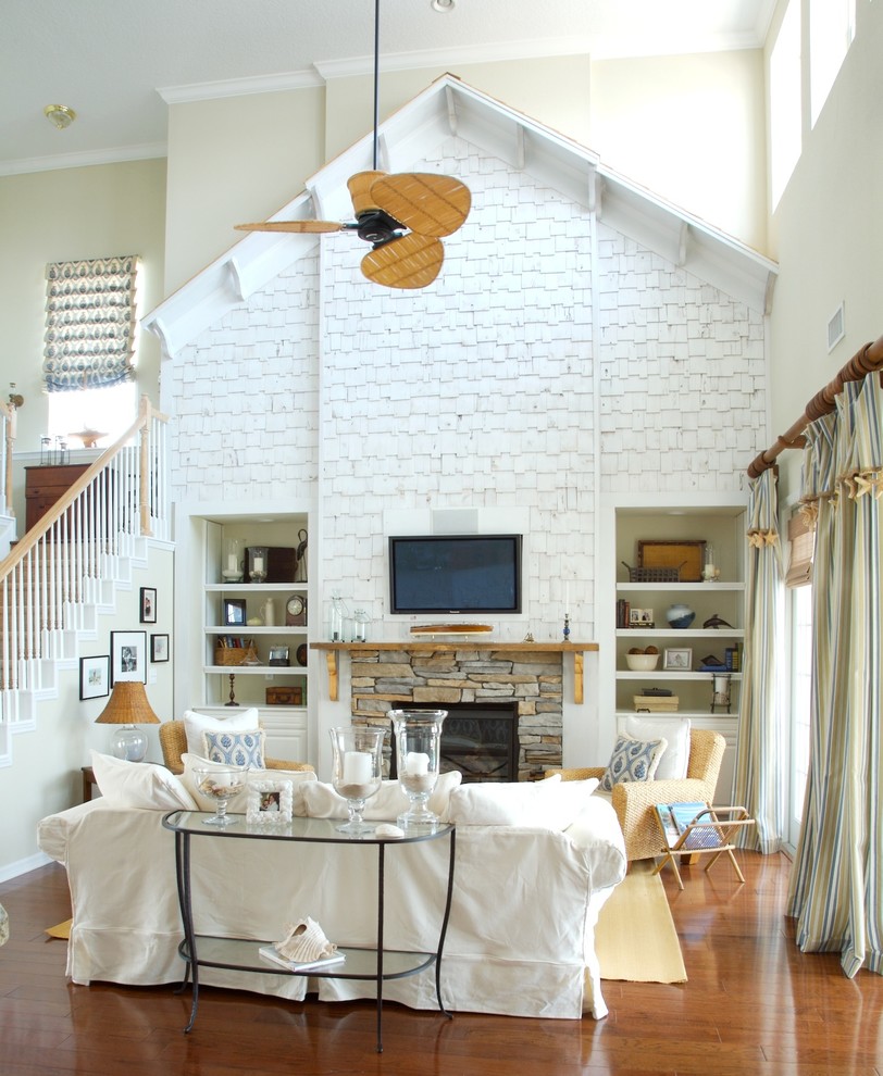 Пример оригинального дизайна: гостиная комната среднего размера в морском стиле с фасадом камина из камня, бежевыми стенами, темным паркетным полом, стандартным камином, телевизором на стене и коричневым полом