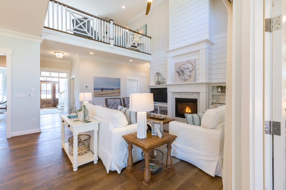 Exemple d'une grande salle de séjour ouverte avec un mur blanc, un sol en bois brun, une cheminée standard, un manteau de cheminée en pierre, un téléviseur encastré et un sol blanc.