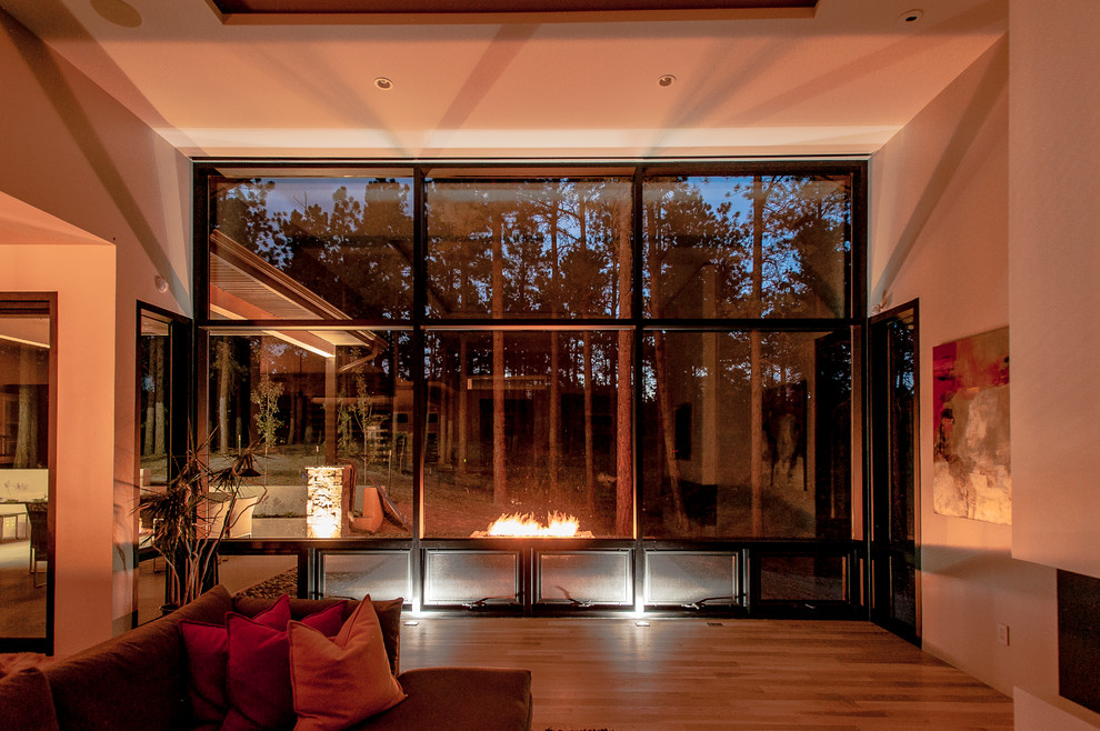 Modelo de sala de estar abierta contemporánea de tamaño medio sin televisor con paredes blancas, suelo de madera clara, chimenea lineal, marco de chimenea de yeso y suelo beige