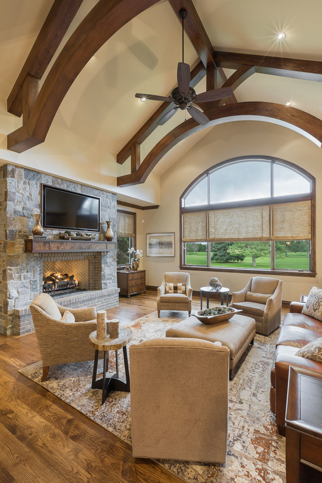 Inspiration for a timeless open concept medium tone wood floor and brown floor family room remodel in Denver with beige walls, a standard fireplace, a stone fireplace and a wall-mounted tv