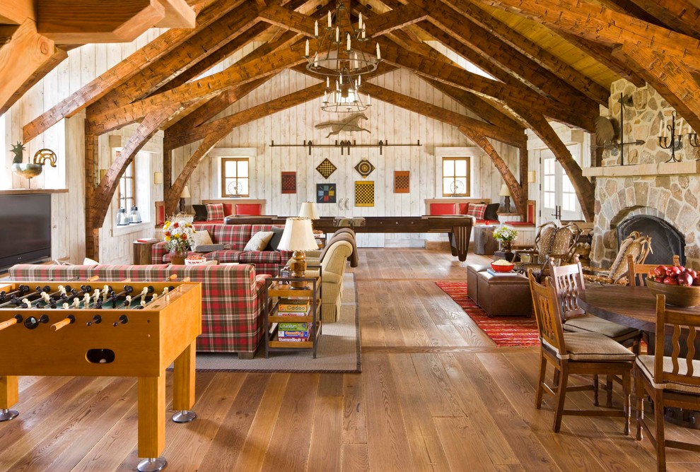 Imagen de sala de estar abierta rural con suelo de madera en tonos medios, todas las chimeneas, televisor independiente y marco de chimenea de piedra