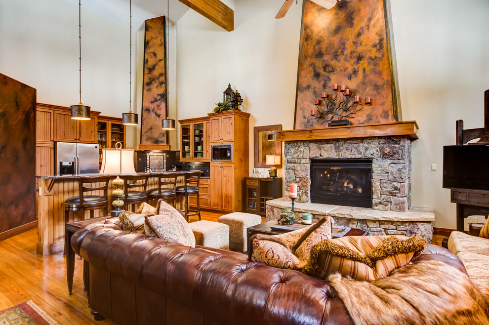 Example of a mid-sized mountain style open concept medium tone wood floor family room design in Denver with a standard fireplace, a stone fireplace and a corner tv