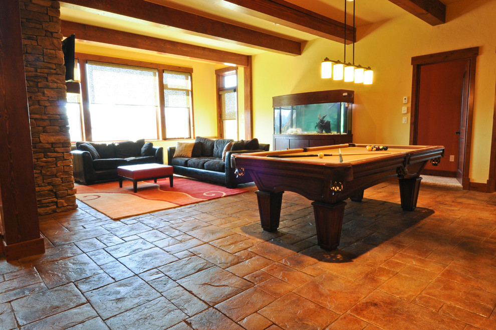 На фото: большая открытая комната для игр в стиле рустика с бежевыми стенами, полом из керамической плитки, стандартным камином, фасадом камина из камня, телевизором на стене и коричневым полом