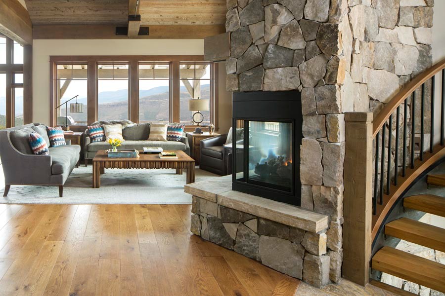 Example of a mid-sized mountain style open concept medium tone wood floor, brown floor and wood ceiling family room design in Denver with beige walls, a two-sided fireplace and a stone fireplace