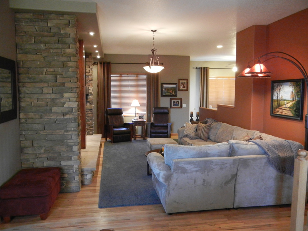 Réalisation d'une salle de séjour tradition ouverte et de taille moyenne avec un mur orange, un sol en bois brun, une cheminée standard, un manteau de cheminée en pierre et un téléviseur fixé au mur.