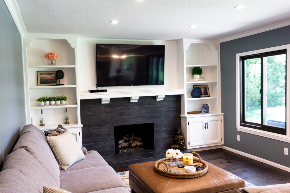 На фото: большая открытая гостиная комната в современном стиле с серыми стенами, темным паркетным полом, стандартным камином, фасадом камина из плитки, телевизором на стене и коричневым полом