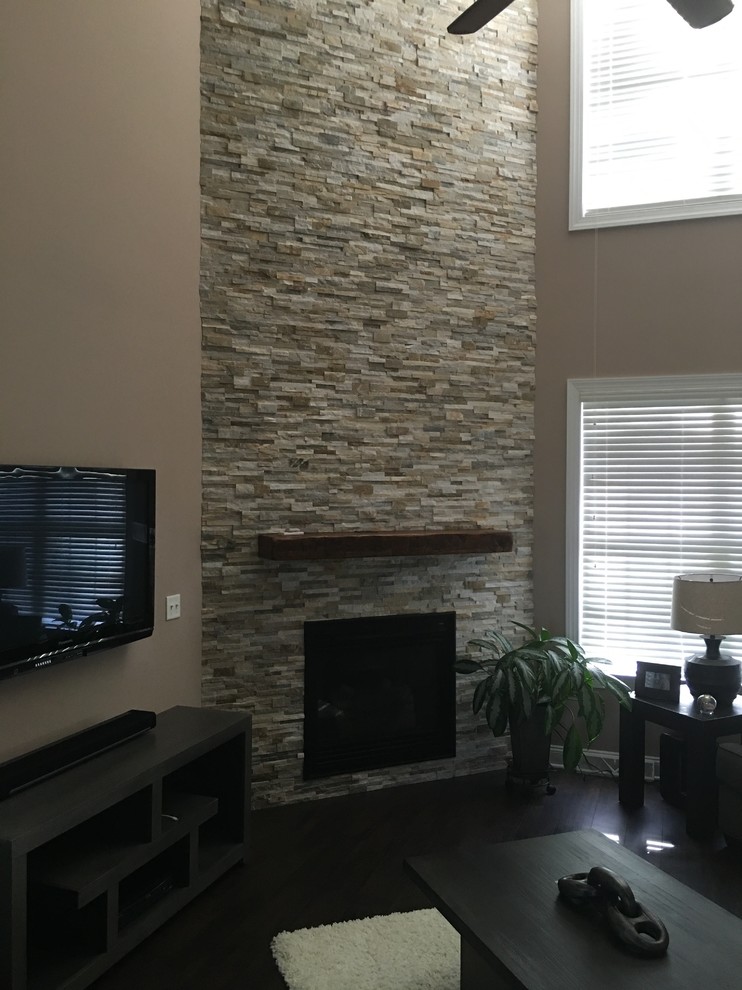 Imagen de sala de estar abierta tradicional renovada de tamaño medio con paredes beige, suelo de madera oscura, chimenea de esquina, marco de chimenea de piedra y televisor colgado en la pared