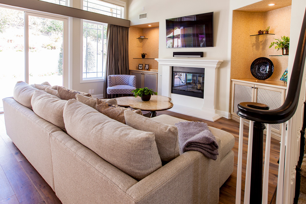 Example of a mid-sized classic open concept medium tone wood floor family room design in San Diego with beige walls, a hanging fireplace, a plaster fireplace and a wall-mounted tv