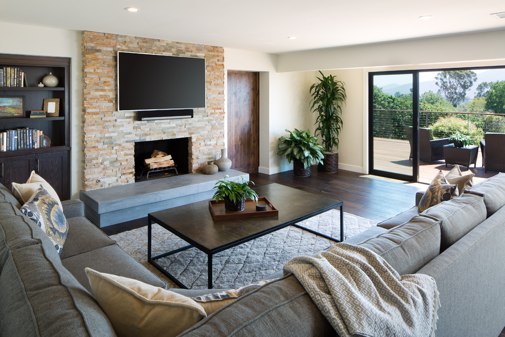 Modelo de sala de estar abierta contemporánea con paredes beige, suelo de madera oscura, todas las chimeneas, marco de chimenea de piedra y televisor colgado en la pared