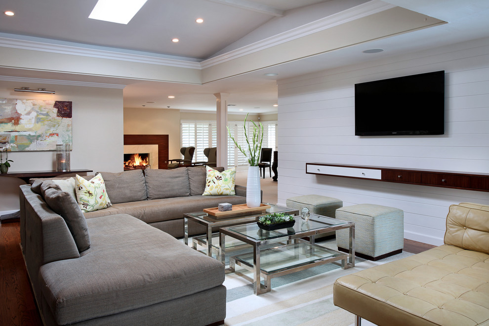На фото: открытая гостиная комната в современном стиле с белыми стенами, темным паркетным полом, телевизором на стене и коричневым диваном