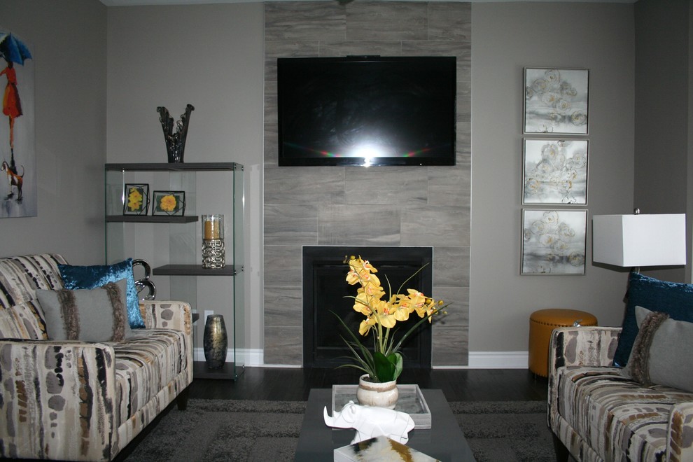 Mittelgroßes, Offenes Modernes Wohnzimmer mit grauer Wandfarbe, dunklem Holzboden, Kamin, gefliester Kaminumrandung, TV-Wand und grauem Boden in Ottawa