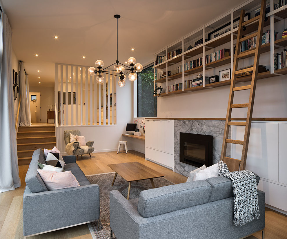 Example of a mid-sized trendy medium tone wood floor and brown floor family room library design in Auckland with white walls, a standard fireplace, a stone fireplace and a concealed tv