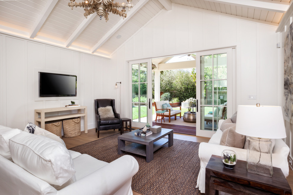 Ejemplo de sala de estar campestre con paredes blancas, suelo de madera en tonos medios y pared multimedia