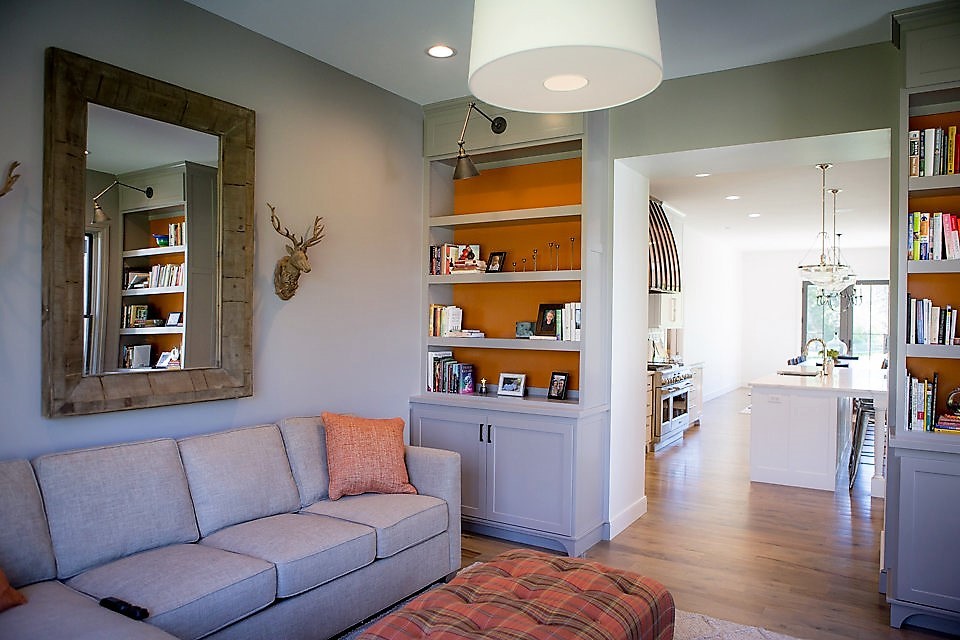 Diseño de sala de estar con biblioteca cerrada campestre de tamaño medio con paredes grises, suelo de madera en tonos medios, televisor colgado en la pared y suelo marrón
