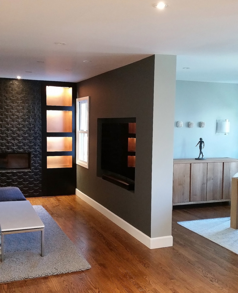 Imagen de sala de estar con biblioteca abierta actual grande con paredes grises, suelo de madera en tonos medios, chimenea lineal, marco de chimenea de hormigón y pared multimedia