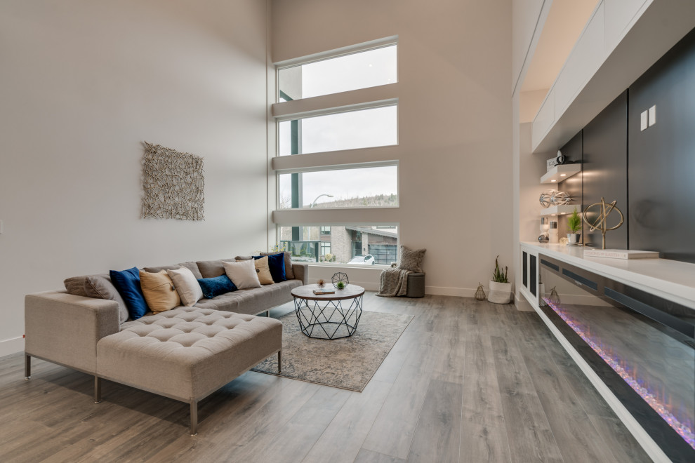 Cette photo montre une salle de séjour tendance de taille moyenne et ouverte avec un mur blanc, sol en stratifié, cheminée suspendue, un manteau de cheminée en bois, un téléviseur encastré et un sol gris.