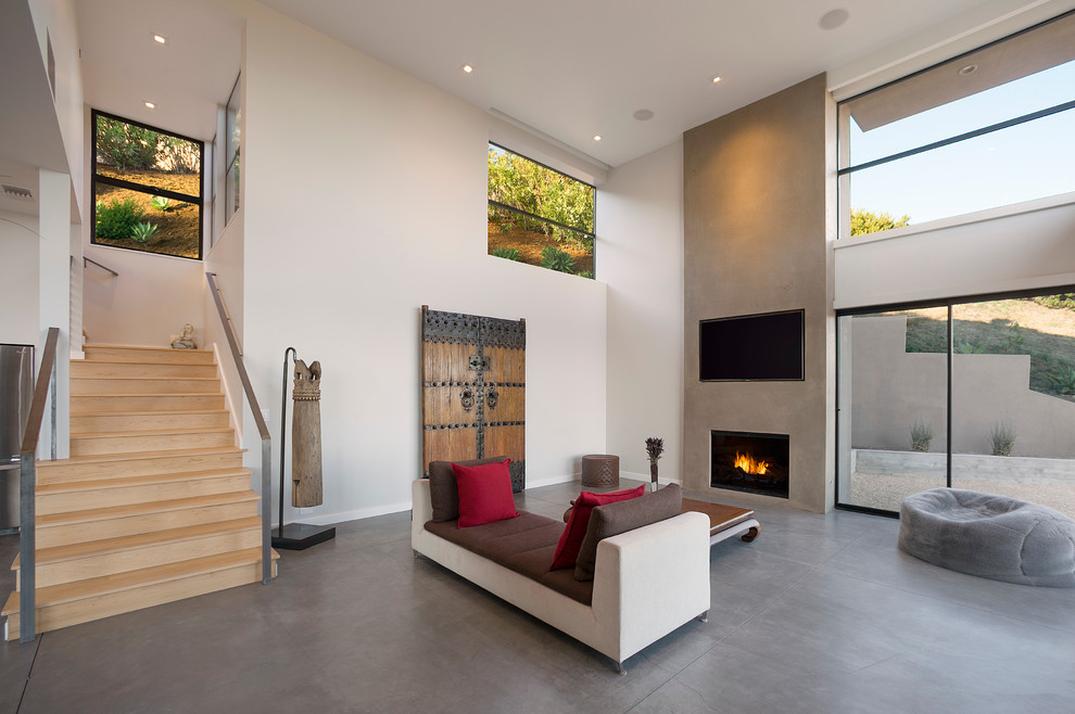 Стильный дизайн: открытая гостиная комната в современном стиле с белыми стенами, бетонным полом, стандартным камином и телевизором на стене - последний тренд