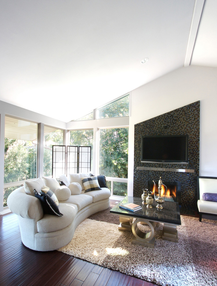 Inspiration for an expansive contemporary open plan games room in Los Angeles with a tiled fireplace surround, medium hardwood flooring, a standard fireplace, a wall mounted tv and white walls.