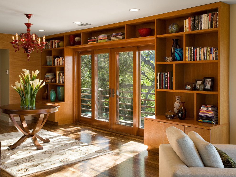Cette photo montre une salle de séjour tendance avec une bibliothèque ou un coin lecture, un mur beige et un sol en bois brun.