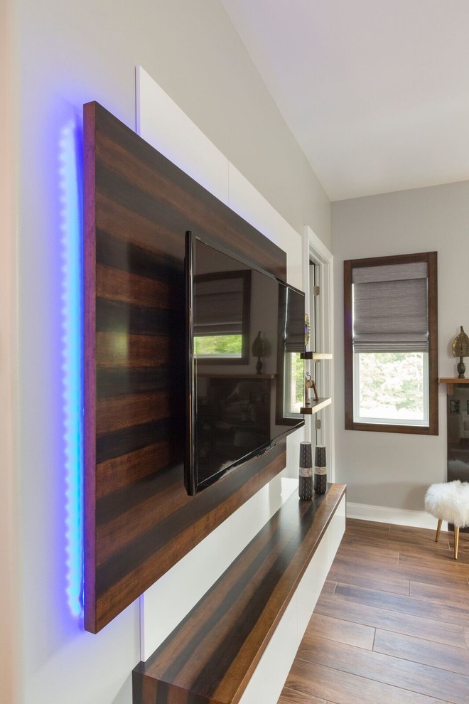 Modern inredning av ett stort allrum med öppen planlösning, med en hemmabar, grå väggar, mellanmörkt trägolv, en väggmonterad TV och brunt golv