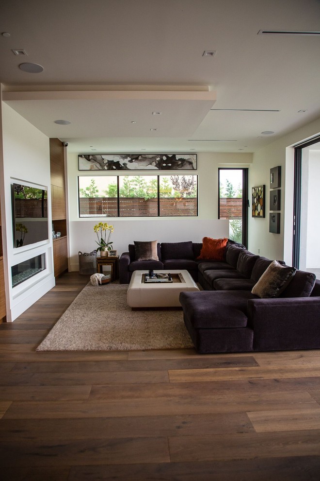 Ejemplo de sala de estar abierta actual grande con paredes blancas, suelo de madera en tonos medios, chimenea lineal, televisor colgado en la pared y suelo marrón