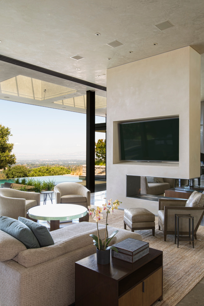 Modelo de sala de estar abierta minimalista extra grande con paredes beige, chimenea de doble cara, marco de chimenea de yeso y televisor colgado en la pared