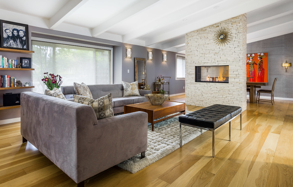 Diseño de sala de estar cerrada retro grande con suelo de madera clara, chimenea de doble cara, marco de chimenea de piedra y paredes púrpuras