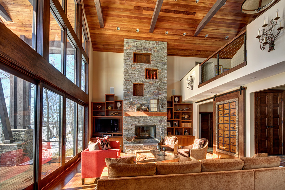Modelo de sala de estar rústica de tamaño medio con paredes beige, suelo de madera en tonos medios, todas las chimeneas, marco de chimenea de piedra y pared multimedia
