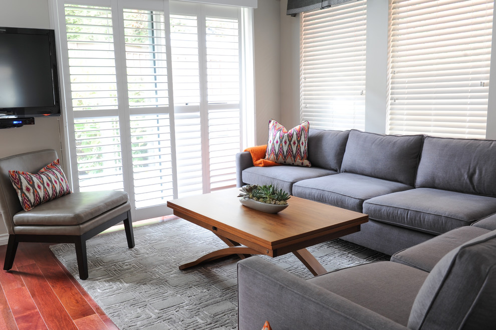 Modelo de sala de estar abierta actual pequeña sin chimenea con paredes grises, suelo de madera en tonos medios y televisor colgado en la pared