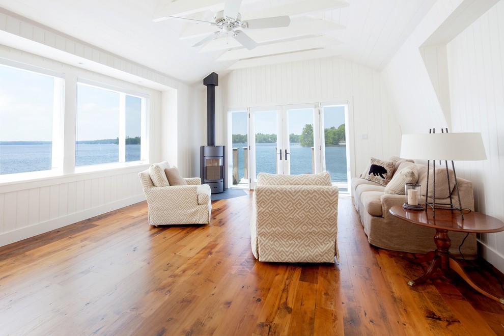 Cette photo montre une salle de séjour mansardée ou avec mezzanine bord de mer de taille moyenne avec un mur blanc, un poêle à bois et un sol marron.