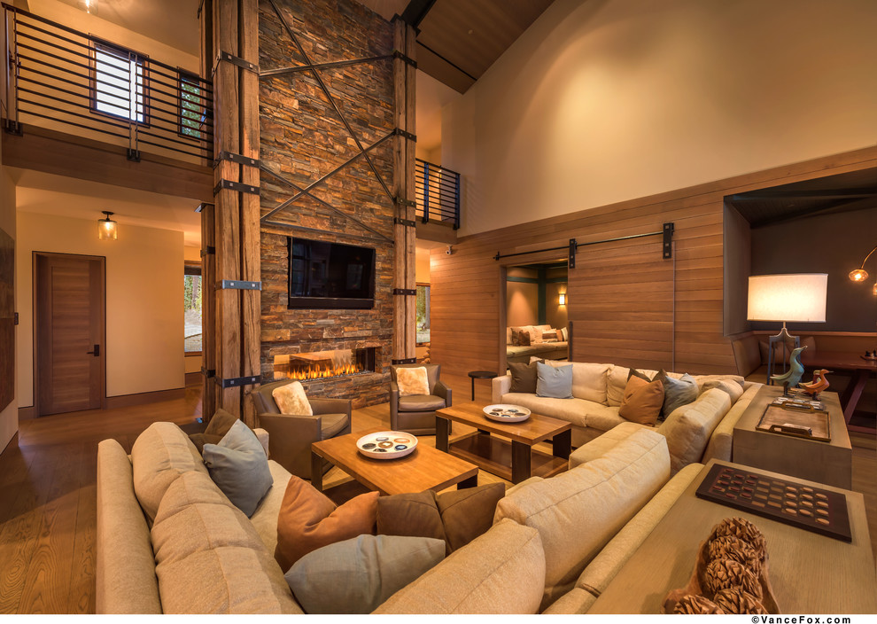 Modelo de sala de estar abierta contemporánea de tamaño medio con paredes beige, suelo de madera en tonos medios, chimenea lineal, marco de chimenea de piedra y pared multimedia