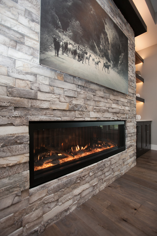 Inspiration pour une grande salle de séjour traditionnelle ouverte avec un mur gris, un sol en bois brun, une cheminée standard et un manteau de cheminée en pierre.