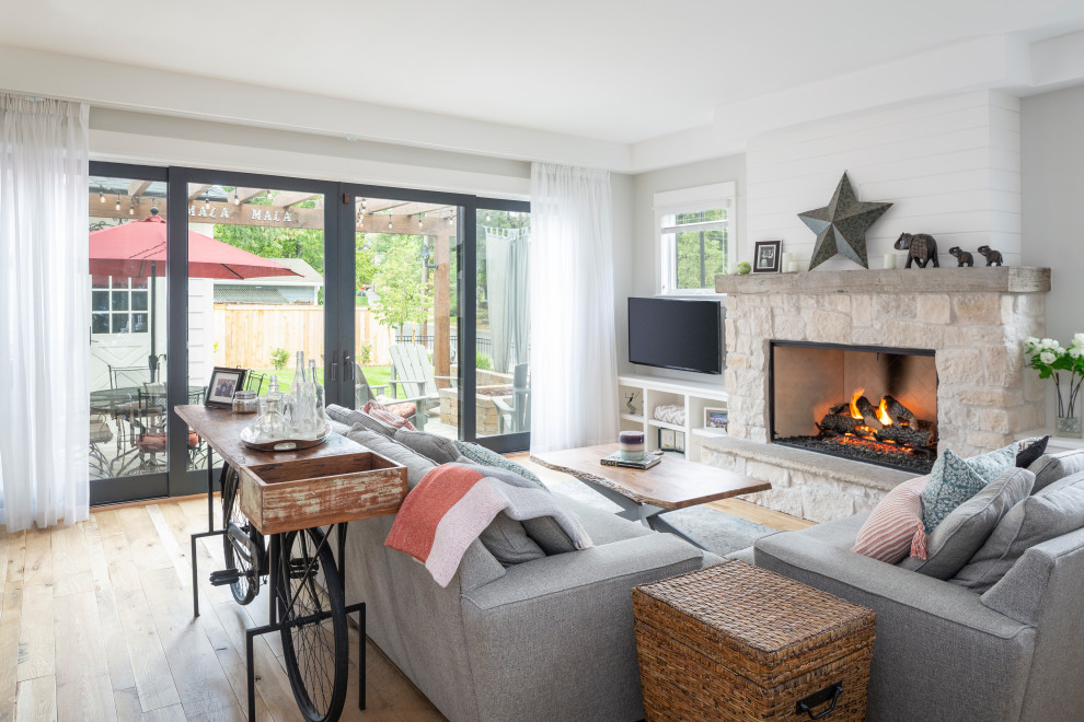 Large country light wood floor and brown floor family room photo in Denver with white walls, a standard fireplace, a stone fireplace and a wall-mounted tv