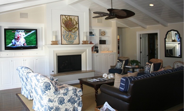 Cette photo montre une salle de séjour bord de mer de taille moyenne et ouverte avec un mur blanc, un sol en bois brun, une cheminée standard, un manteau de cheminée en bois et un téléviseur encastré.