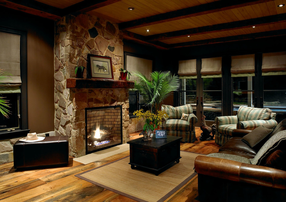 Cette image montre une salle de séjour rustique de taille moyenne et ouverte avec un mur marron, un sol en bois brun, une cheminée standard, un manteau de cheminée en pierre, aucun téléviseur et un sol marron.