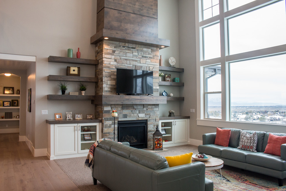 Modelo de sala de estar abierta tradicional de tamaño medio con paredes grises, suelo de madera clara, todas las chimeneas, marco de chimenea de piedra y televisor colgado en la pared