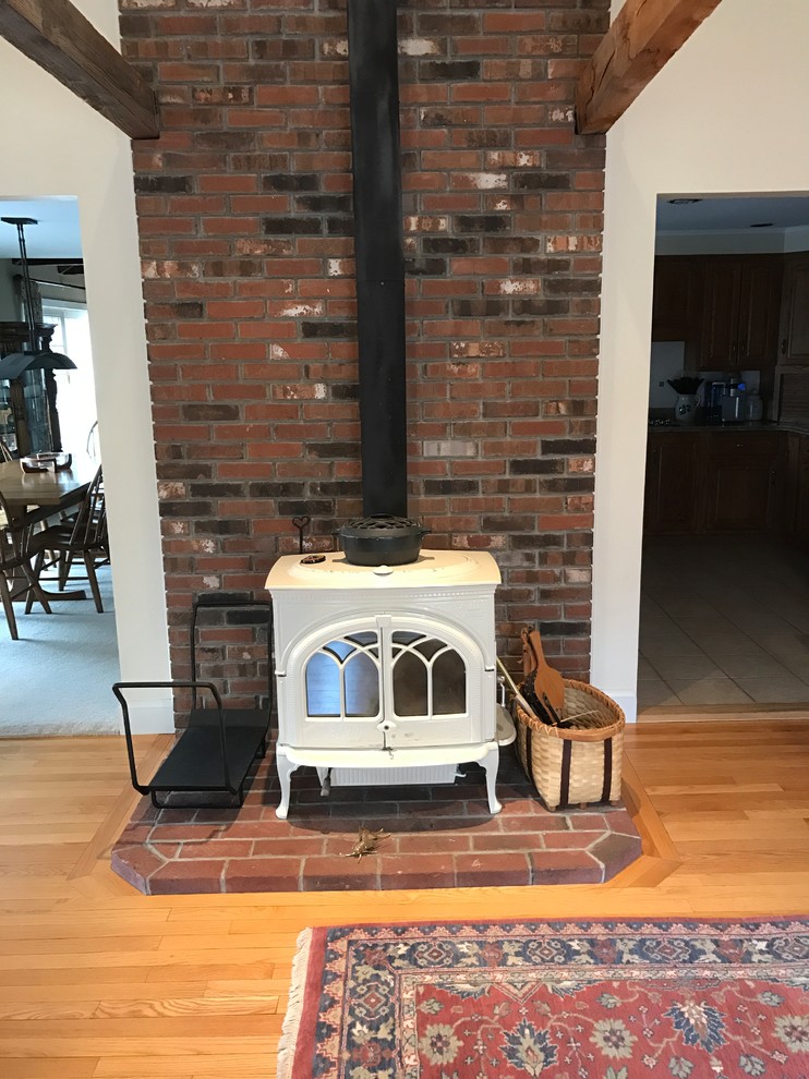 Example of a large trendy light wood floor family room design in Boston with beige walls, a wood stove and a brick fireplace