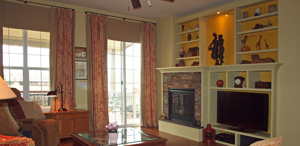 Modelo de sala de estar abierta tradicional de tamaño medio con paredes beige, suelo de madera oscura, todas las chimeneas, marco de chimenea de piedra, televisor independiente y suelo marrón
