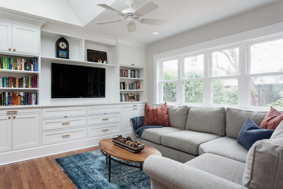Modelo de sala de estar abierta actual de tamaño medio sin chimenea con paredes beige, suelo de madera en tonos medios y pared multimedia