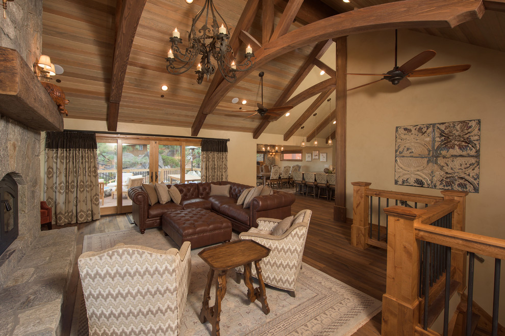 Modelo de sala de estar tipo loft rural grande sin televisor con paredes beige, suelo de madera en tonos medios, todas las chimeneas y marco de chimenea de piedra