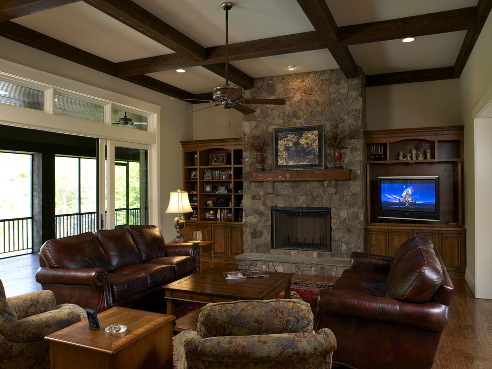 Cette photo montre une salle de séjour craftsman avec un mur beige, parquet foncé, une cheminée standard, un manteau de cheminée en pierre, un téléviseur encastré et éclairage.