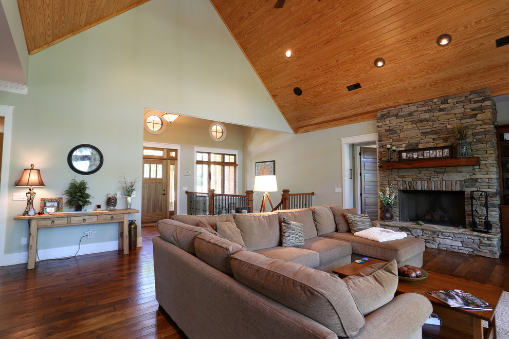 Ejemplo de sala de estar abierta de estilo americano grande sin televisor con paredes beige, suelo de madera en tonos medios, todas las chimeneas y marco de chimenea de piedra
