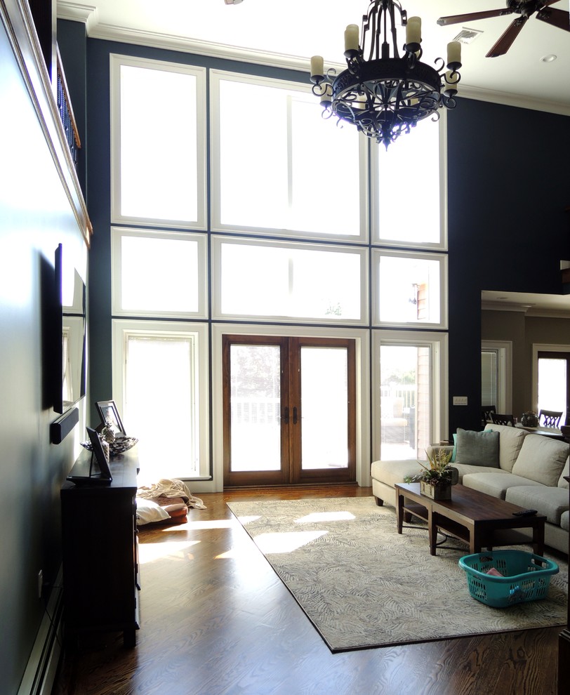 На фото: большая открытая гостиная комната в стиле кантри с синими стенами, темным паркетным полом, телевизором на стене и коричневым полом без камина с