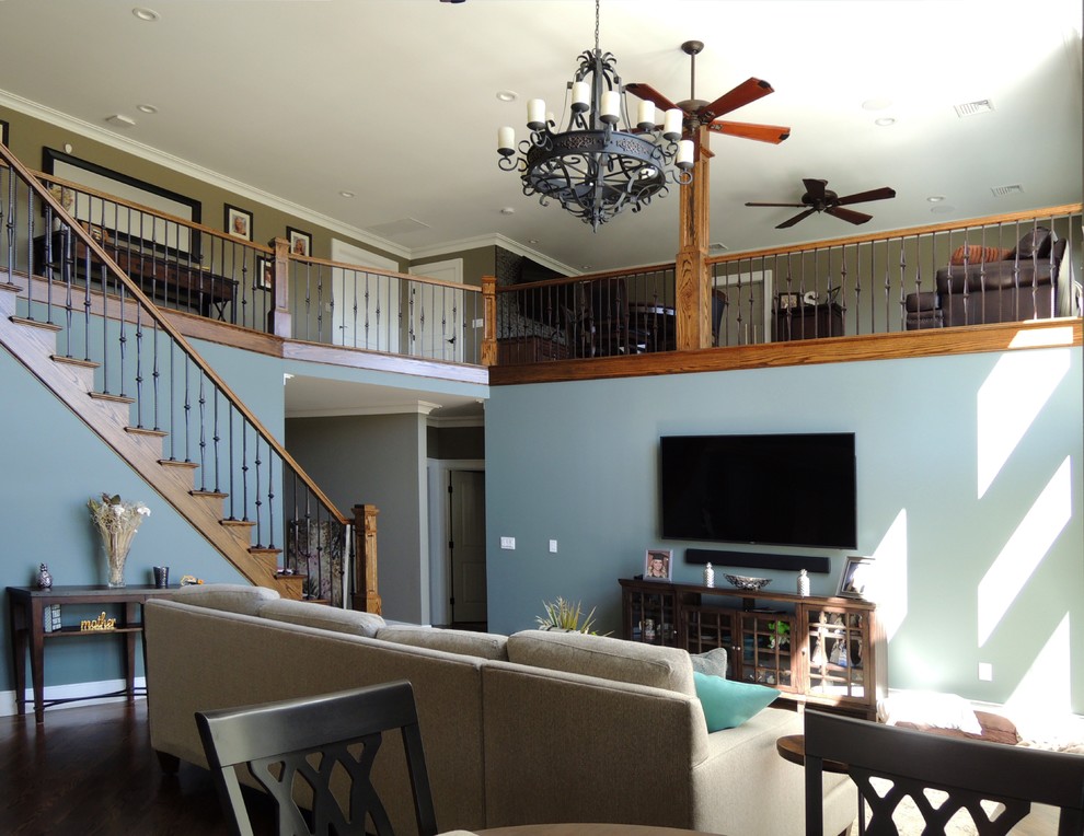 Diseño de sala de estar abierta de estilo americano grande sin chimenea con paredes azules, suelo de madera oscura, televisor colgado en la pared y suelo marrón
