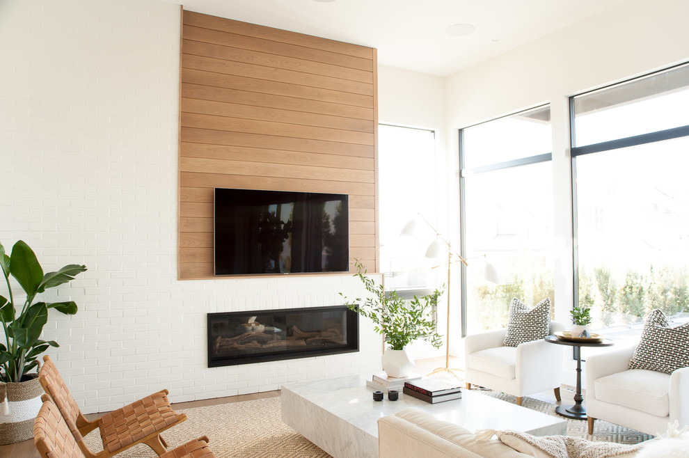 Foto på ett minimalistiskt allrum, med vita väggar, mellanmörkt trägolv, en bred öppen spis, en spiselkrans i tegelsten, en väggmonterad TV och brunt golv