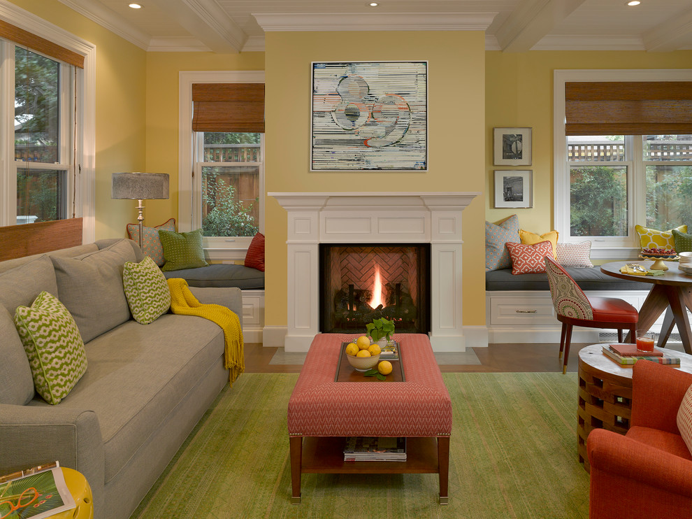 На фото: гостиная комната в стиле неоклассика (современная классика) с желтыми стенами, светлым паркетным полом, стандартным камином и фасадом камина из дерева